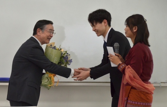 感謝のセレモニーで花束を受け、学生代表と握手する宗次氏